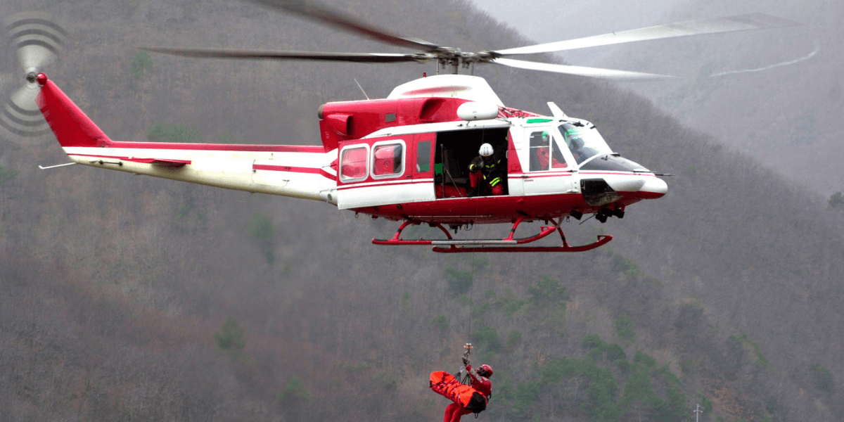 Rescue helicopter hovering above, with a person being lowered in a harness.