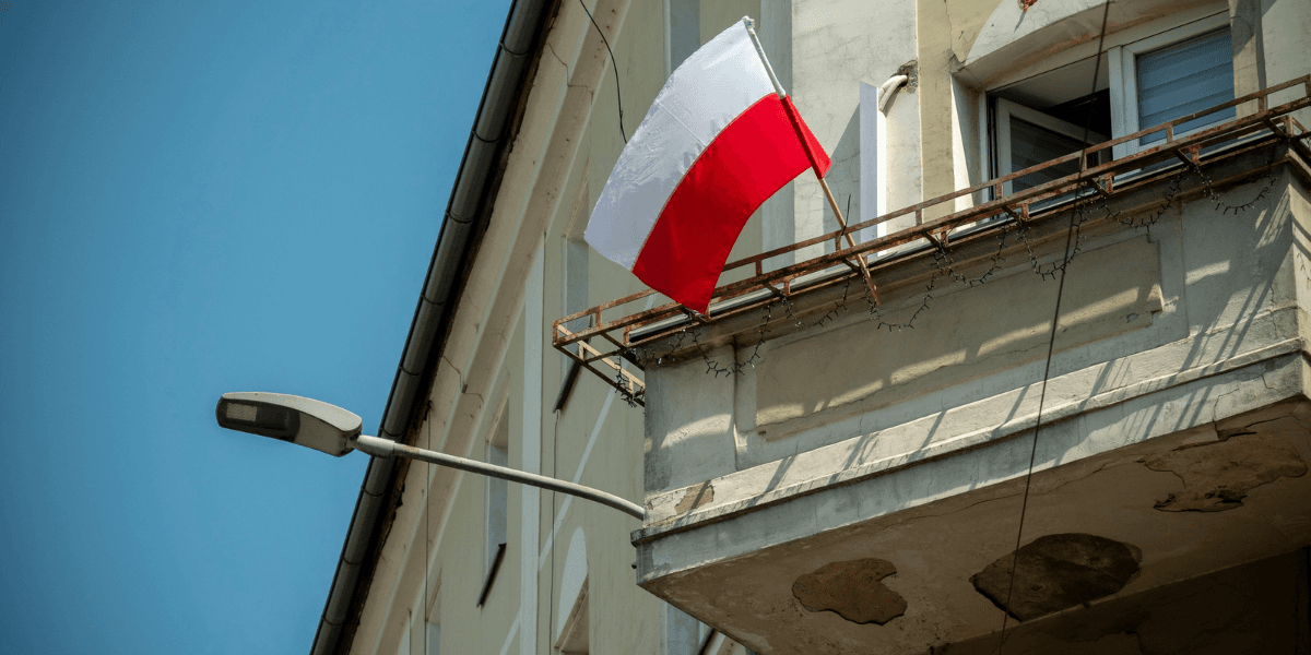 Polish flag hanging from a balcony of a building under a clear blue sky