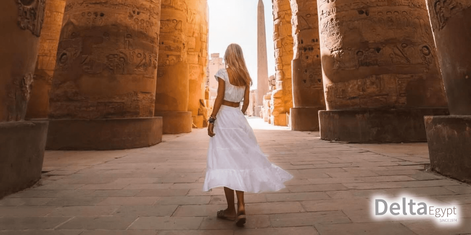 "Woman in a white dress walking through the ancient Egyptian temple ruins with tall columns, featuring the Delta Egypt logo in the corner."
