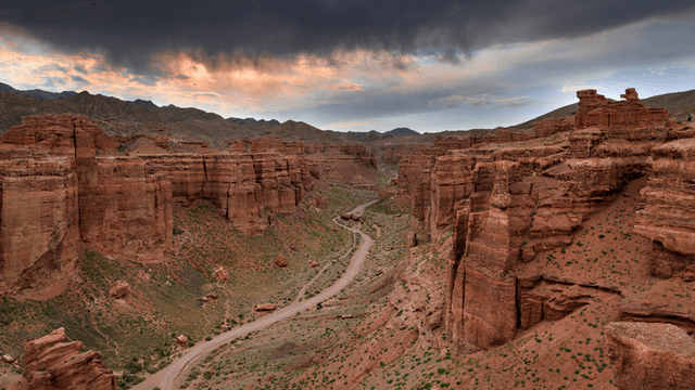 Expansive canyon landscape with dramatic rock formations and a winding dirt road.