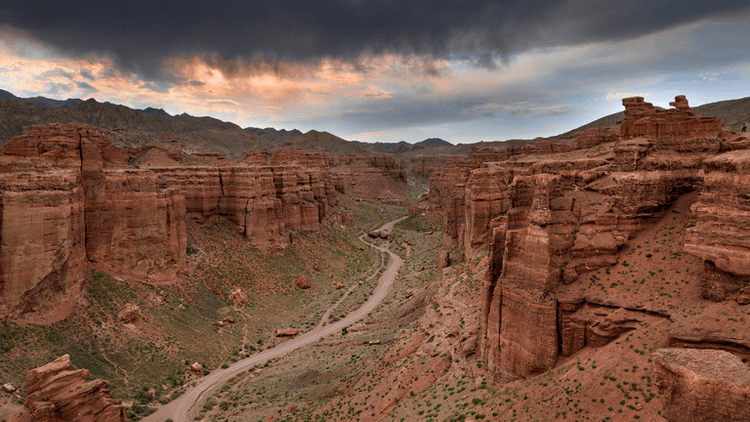 Expansive canyon landscape with dramatic rock formations and a winding dirt road.