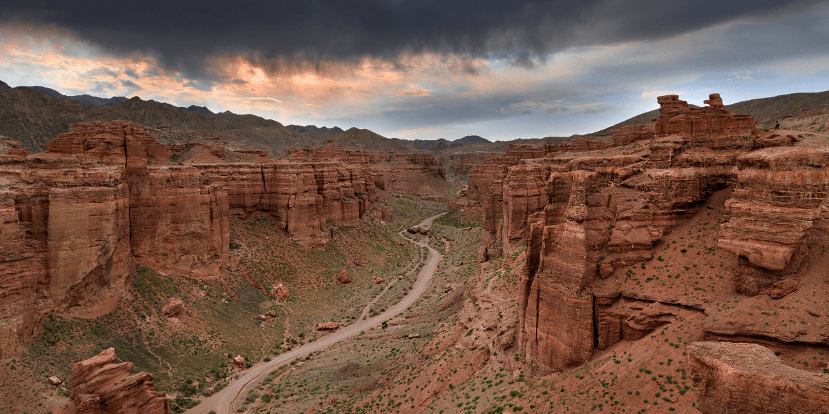 Expansive canyon landscape with dramatic rock formations and a winding dirt road.