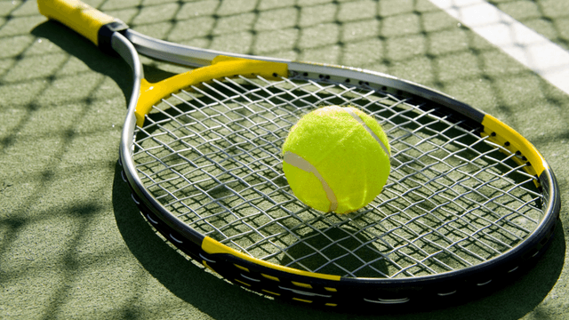 Tennis racket on a court with a tennis ball resting on the strings
