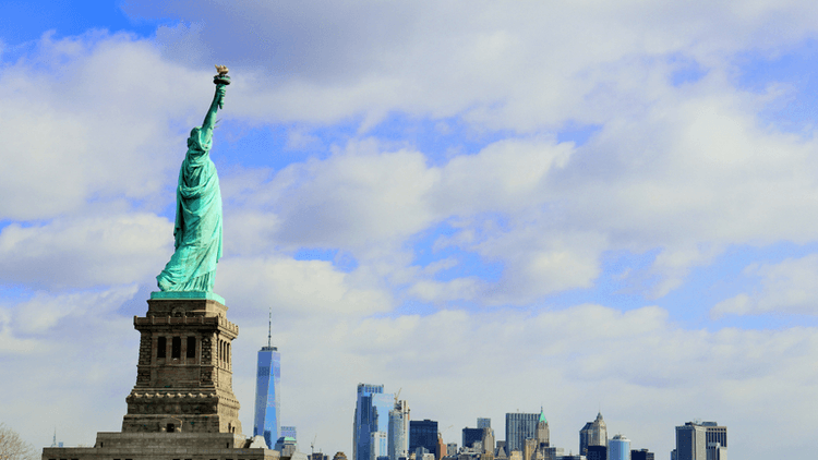 Statue of Liberty with Manhattan skyline and cloudy blue sky in the background
