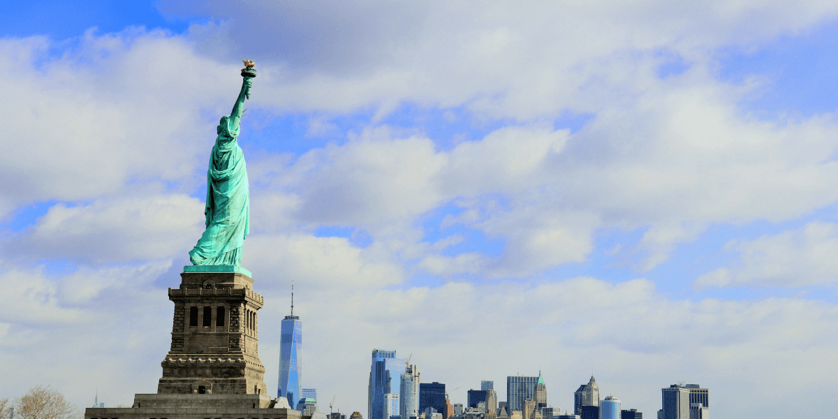 Statue of Liberty with Manhattan skyline and cloudy blue sky in the background