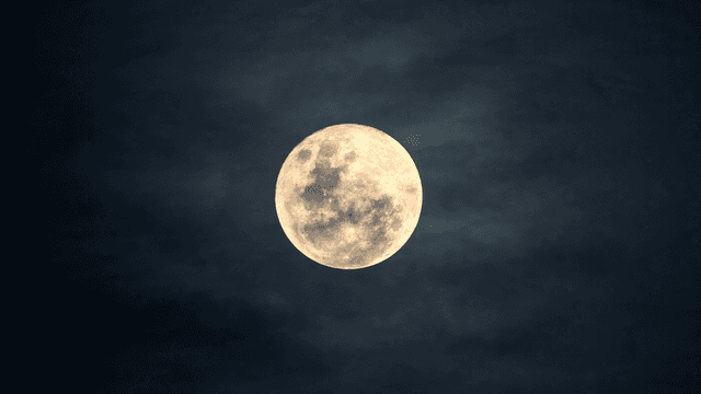 Full moon against a dark sky with subtle cloud textures surrounding it