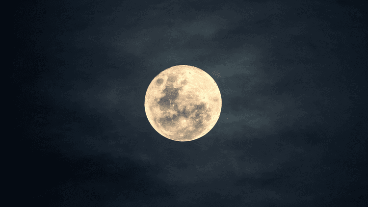 Full moon against a dark sky with subtle cloud textures surrounding it