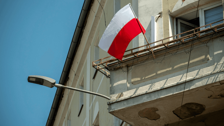 Polish flag hanging from a balcony of a building under a clear blue sky