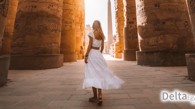 "Woman in a white dress walking through the ancient Egyptian temple ruins with tall columns, featuring the Delta Egypt logo in the corner."
