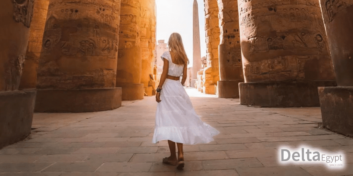 "Woman in a white dress walking through the ancient Egyptian temple ruins with tall columns, featuring the Delta Egypt logo in the corner."
