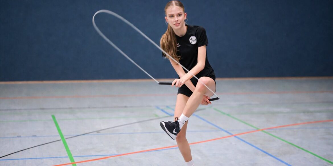 A person in black sports attire skillfully jump ropes indoors on a court. The blue wall and colorful court lines accentuate the action and focus.