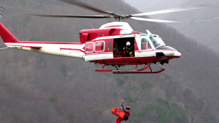 Rescue helicopter hovering above, with a person being lowered in a harness.